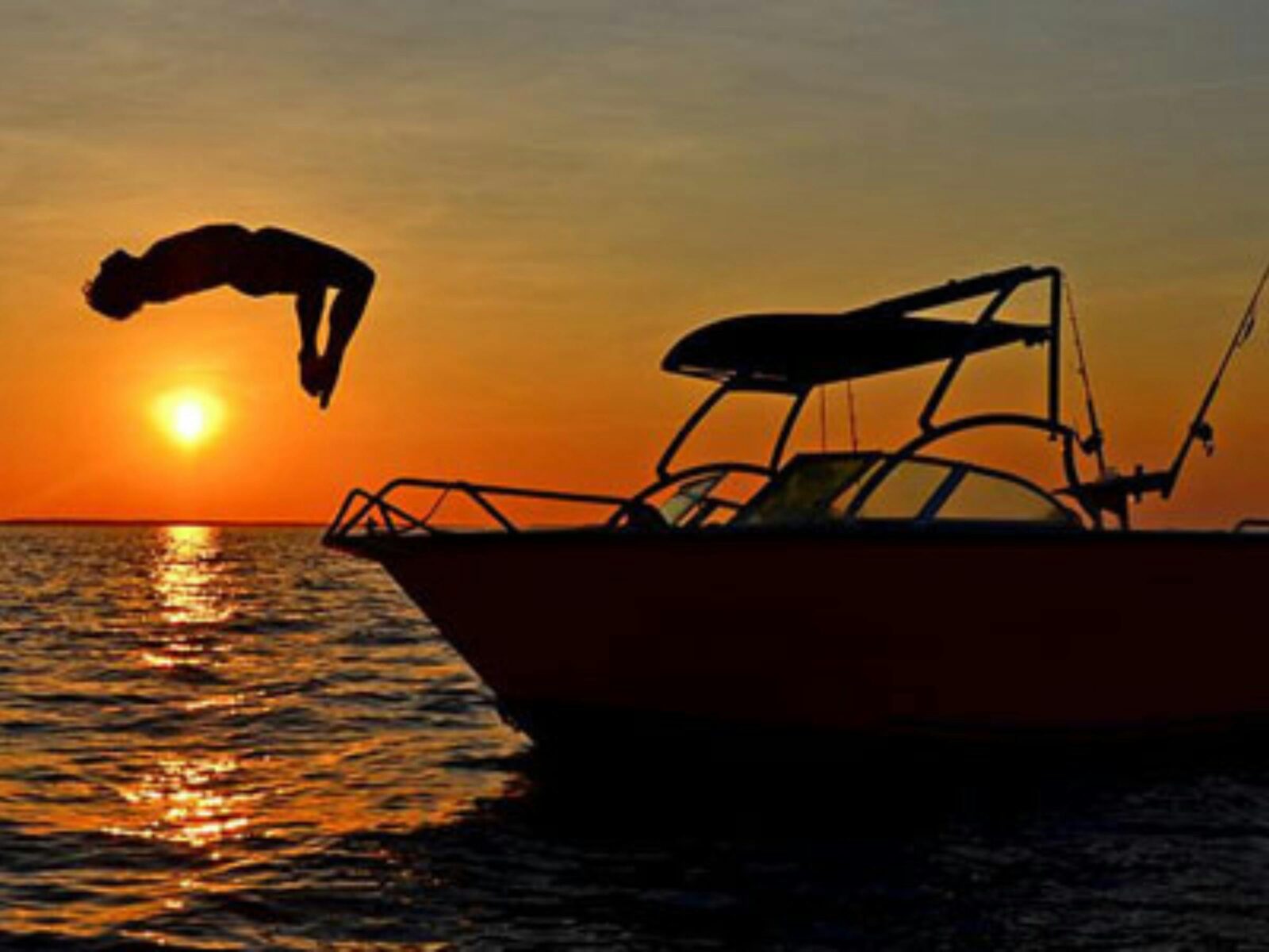 A person doing a backflip off a boat during sunset