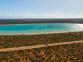 A holiday caravan driving through a red desert landscape, passing Lake Thedham in Shark Bay