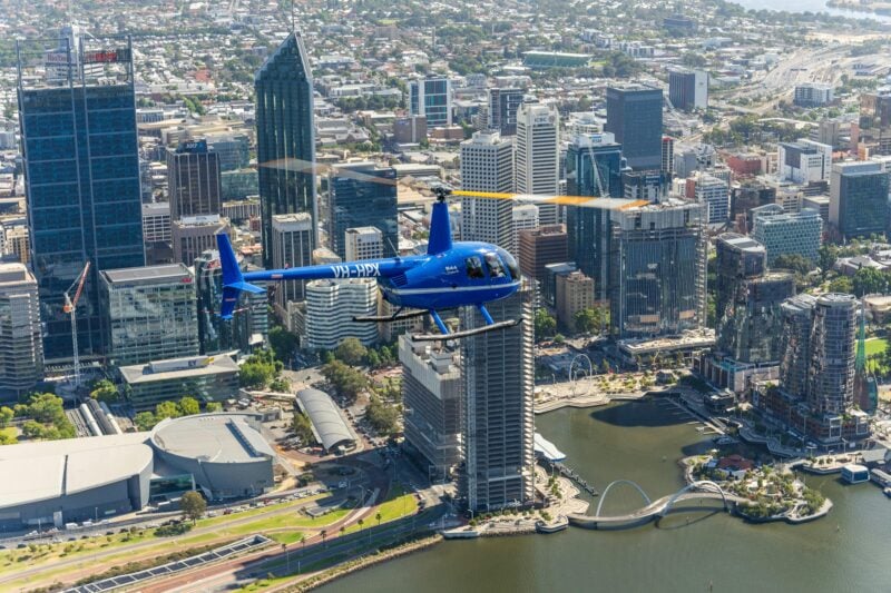 blue Jandakot Heli-Co Robinson R44 helicopter flying over the city of Perth