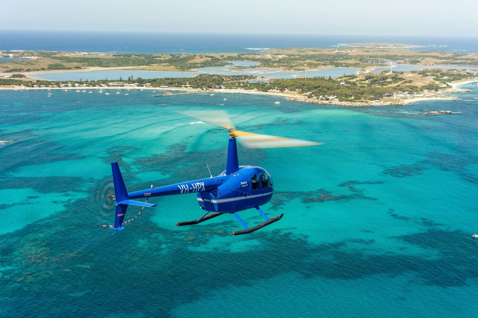 Blue Jandakot Heli-Co Robinson R44 helicopter flying over the ocean to Rottnest Island